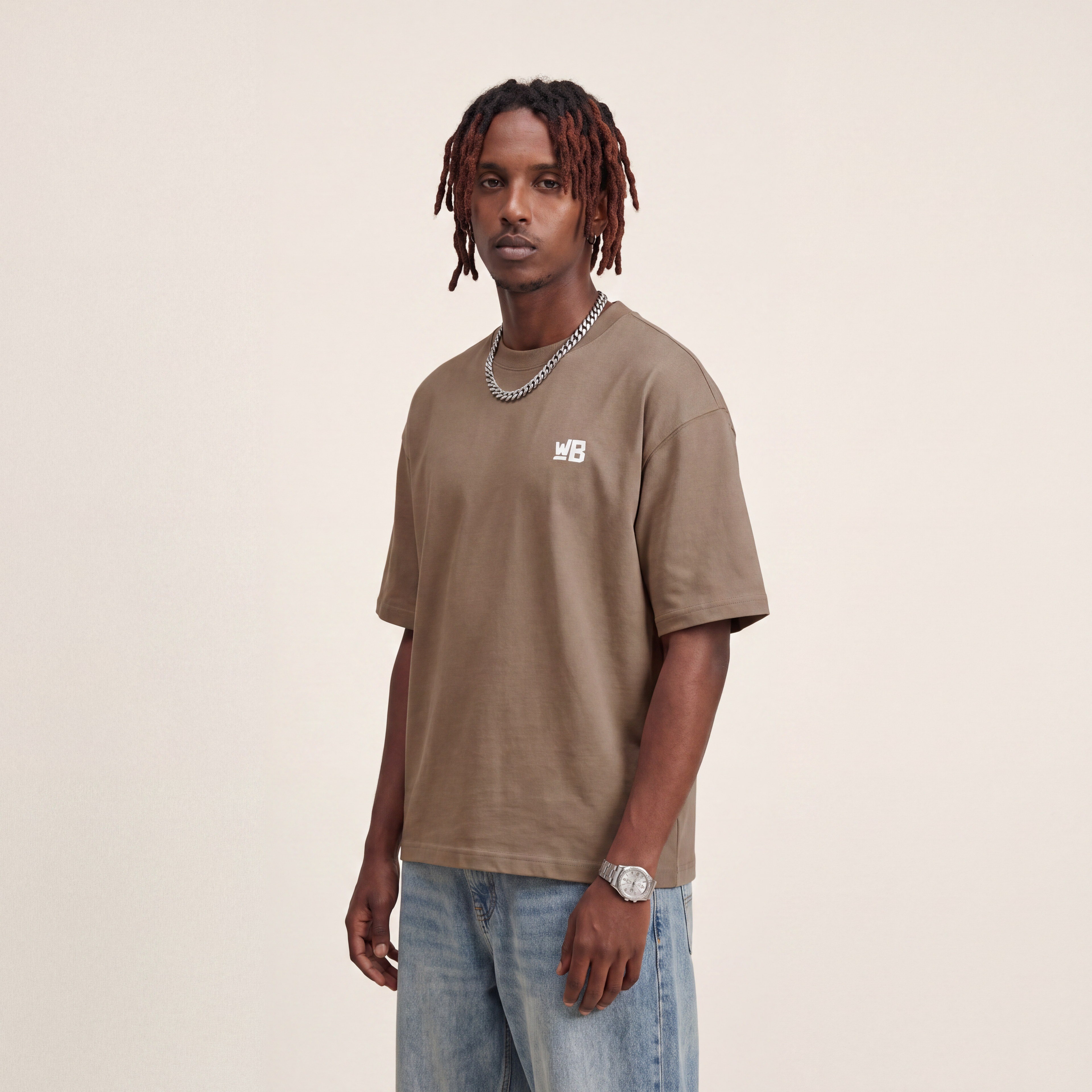 Base Blackness Tee Brown worn by model, front view with WB chest logo on warm ivory studio backdrop