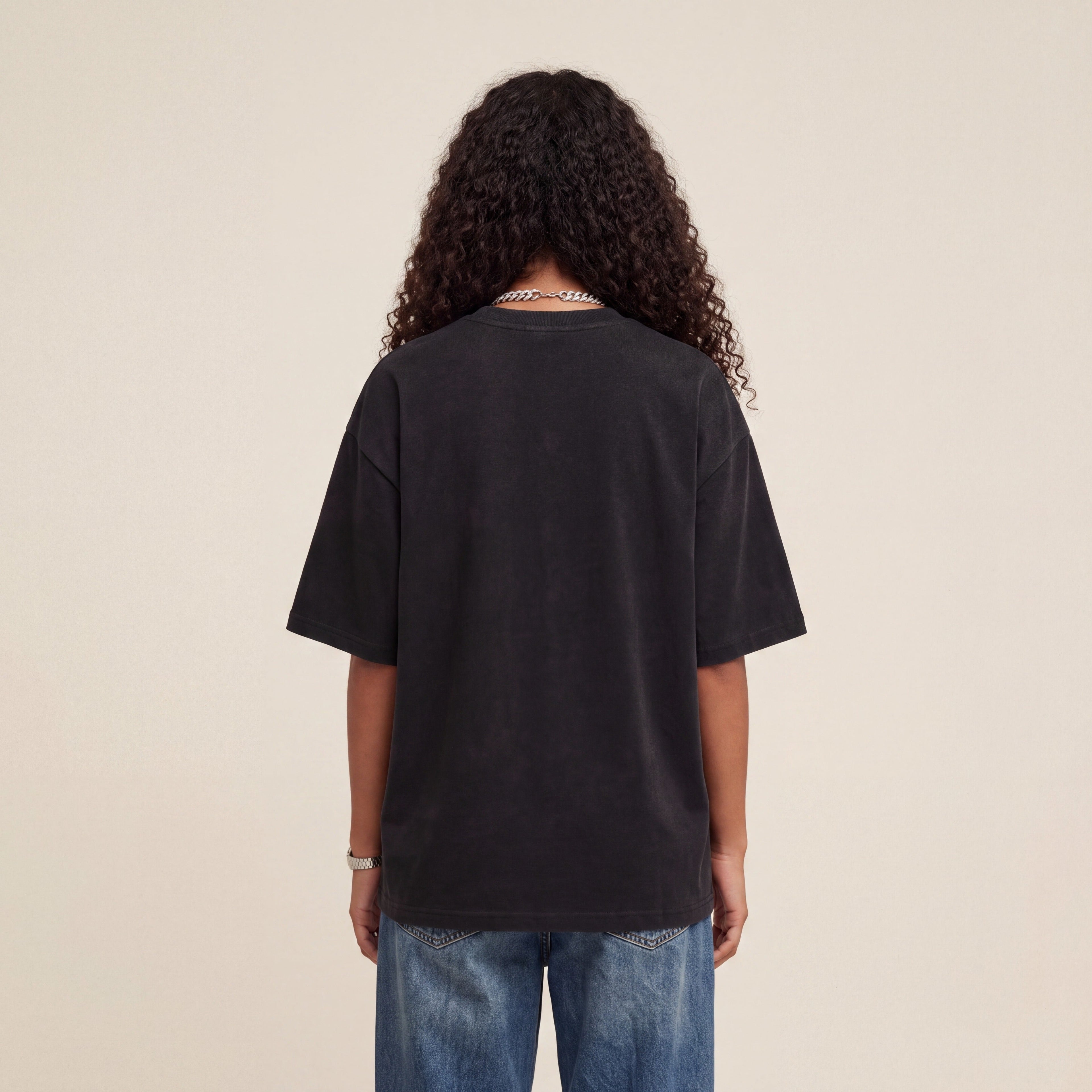 Wear Blackness Tee Black worn by model, back view showing the clean plain back on warm ivory studio backdrop