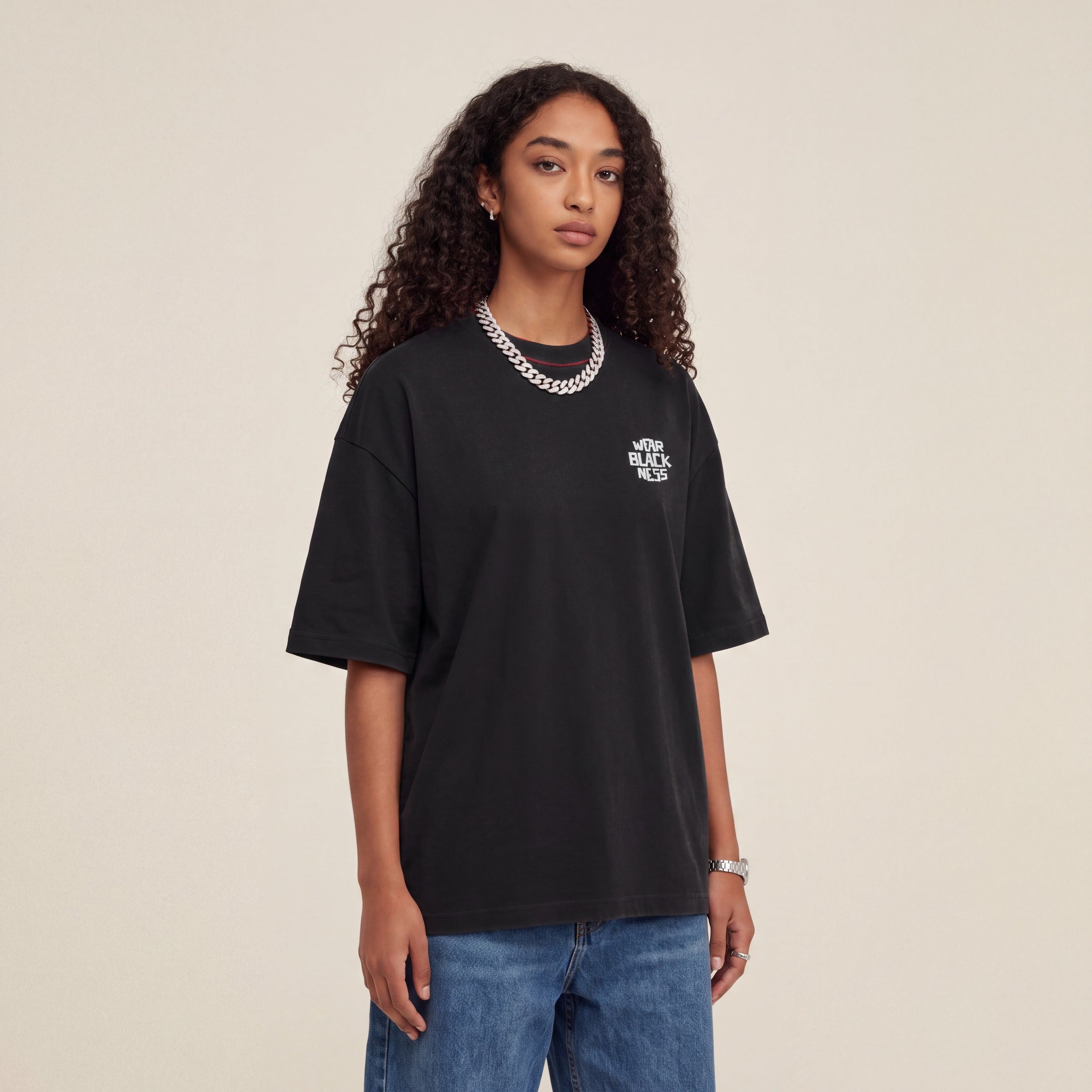 Wear Blackness Tee Black worn by model, front view with Wear Blackness chest print on warm ivory studio backdrop